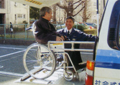 介護員がリフトで乗車する車いすに乗った方を介助している写真
